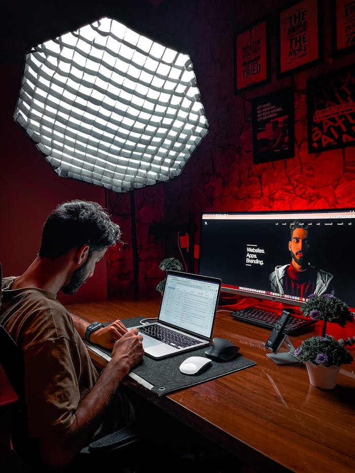 why-choose-us-01 Asian man working at a laptop in a stylish red-lit room with modern equipment and lighting.